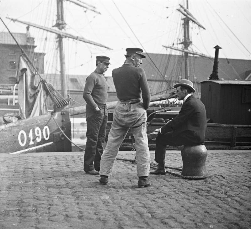 Three men at quay, ships in background