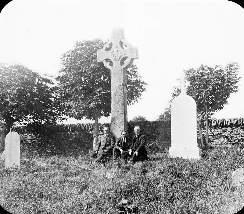 Three men at foot of St. Boyne's Cross, Monasterboice. In situ, in graveyard.