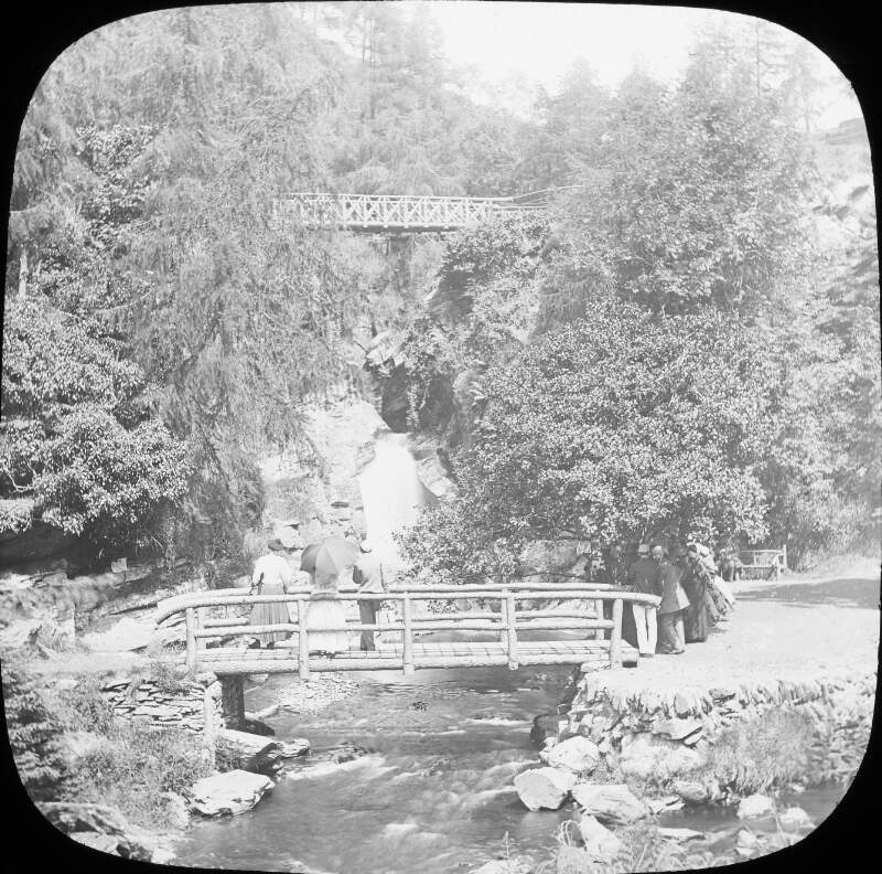 Bridges over a stream, in valley with figures looking on.