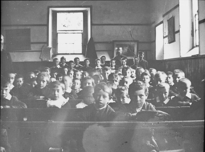 Education, young boys in classroom with teacher/priest to left of frame.