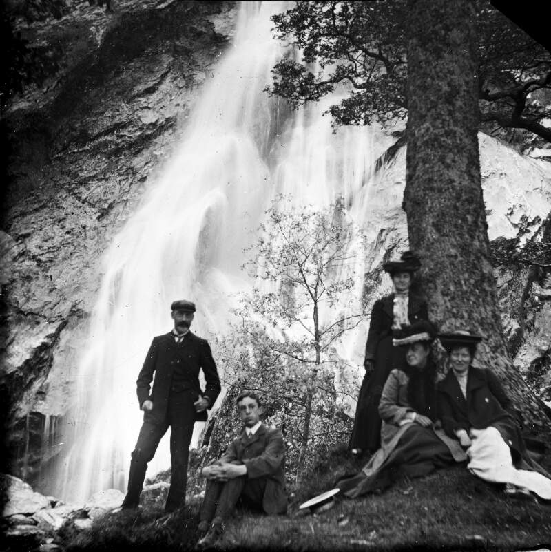 Three women and two men standing at a waterfall.