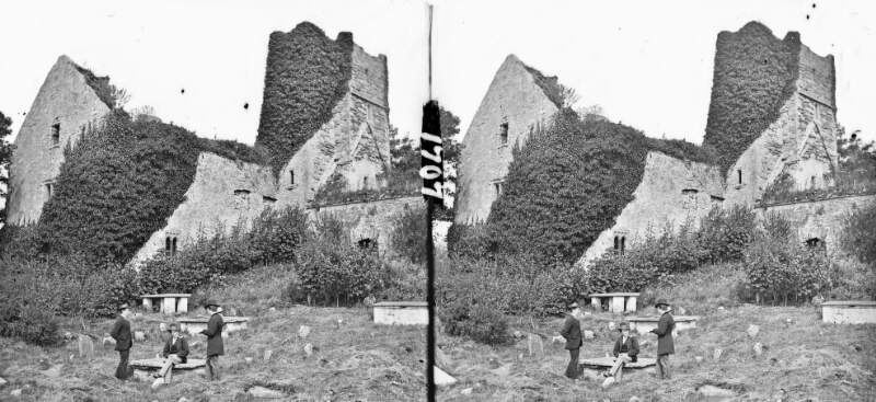 Ruined monastic building, central square tower, graveyard, people in foreground