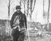 [Eugène Lemercier standing with walking stick in left hand, in the woods, wearing his uniform and scarf and hat]