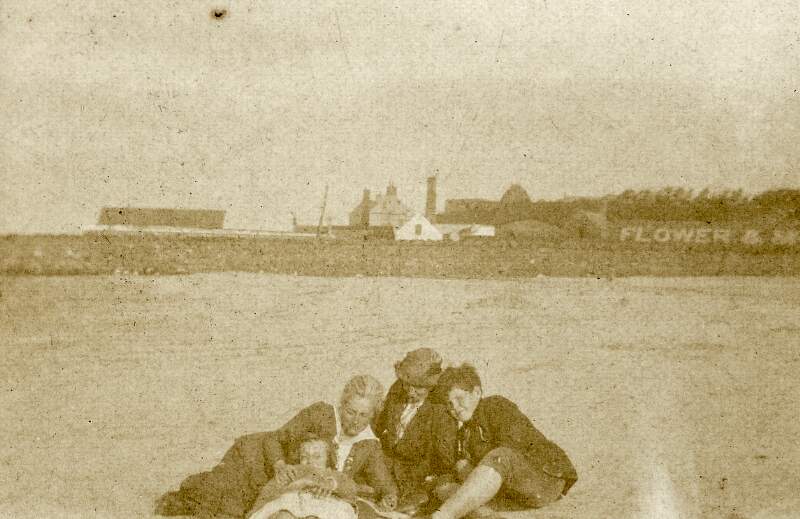 [Áine Ceannt and Ronán Ceannt, with woman and young girl on beach, wall with "Flower & Mc [Donald]" visible in background, possibly Ringsend]
