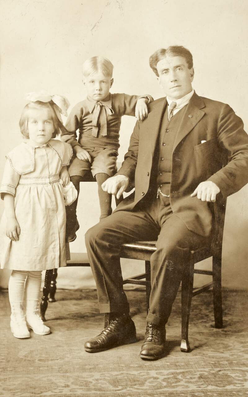 [Man seated, with young boy and girl, full-length studio portrait, facing forward]