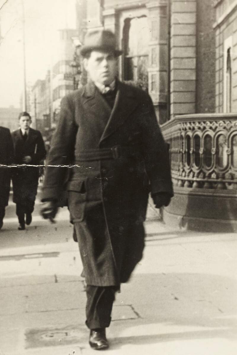 [Ronán Ceannt, in coat and hat walking along street, full-length portrait