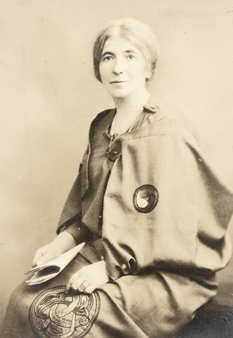 [Áine Ceannt, wearing robe with celtic embroidered design and brooch, seated three-quarter length portrait]