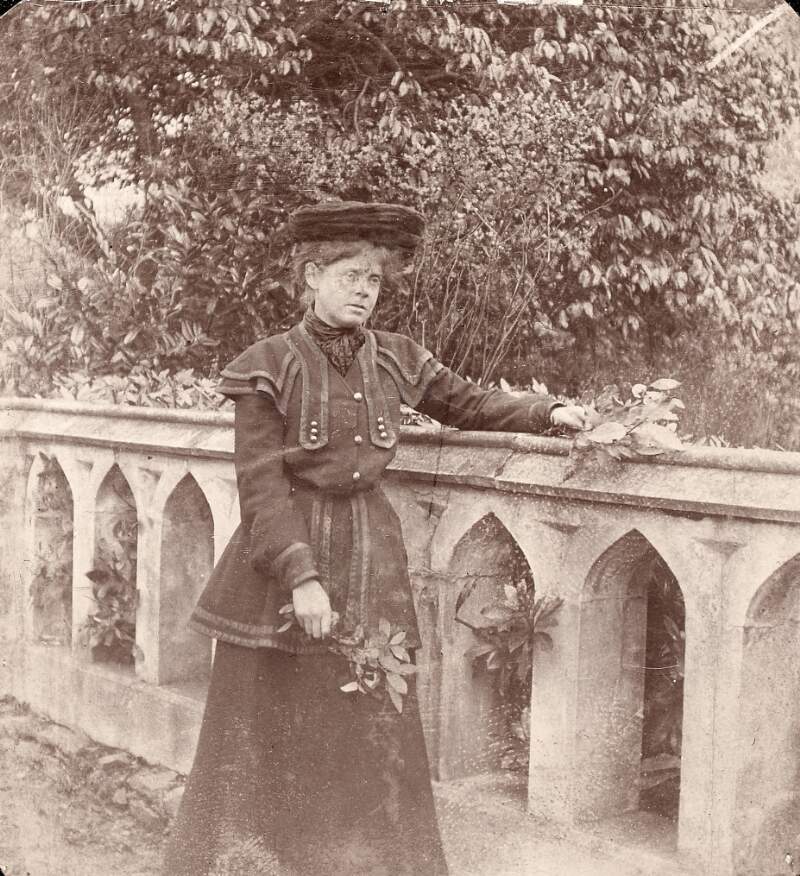 [Alice Milligan, three-quarter length portrait, facing right, standing in rural scene, holding branches]