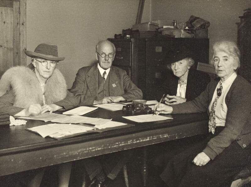 [Áine Ceannt with three others seated at a table, signing documents, seated portrait]