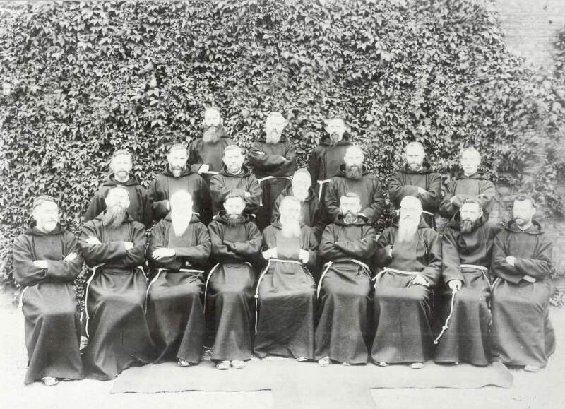 [Group of eighteen unidentified Franciscan friars in front of ivy covered wall, front facing, full-length portrait]