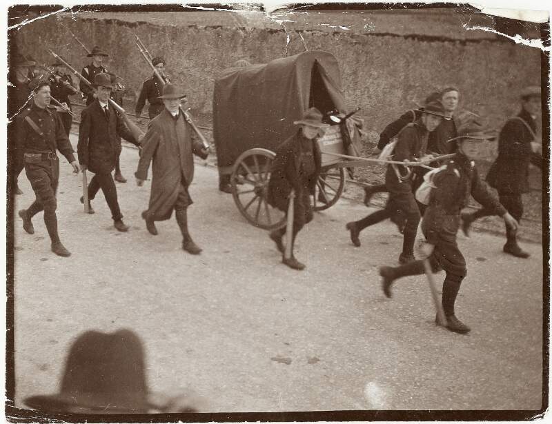 [Unidentified men and boys carrying guns and sticks, and also drawing a cart]