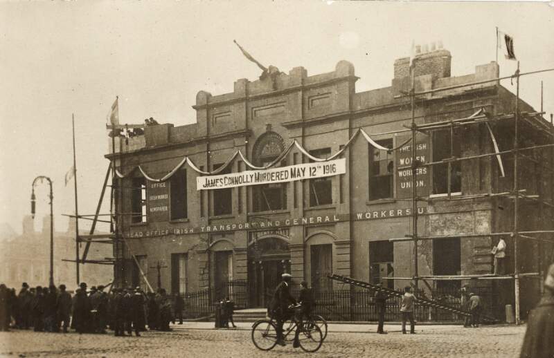 [Front of the head office of the Irish Transport and General Workers Union, Liberty Hall, adorned with banner stating "James Connolly Murdered May 12th 1916", and including onlookers on the street]