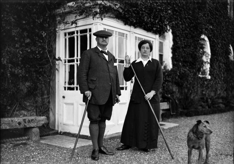 [John Redmond, standing with woman and dog, outside porch]