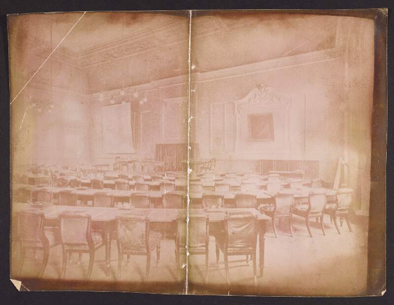 [Rows of chairs and desks, with ink wells and pens, facing a raised platform. Location unidentified] .