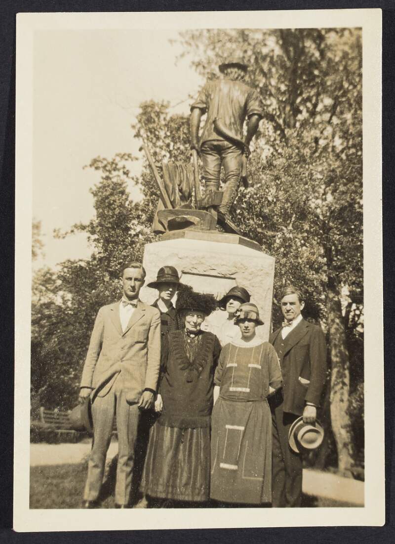 [Two men and four women standing at a monument of a ploughman]