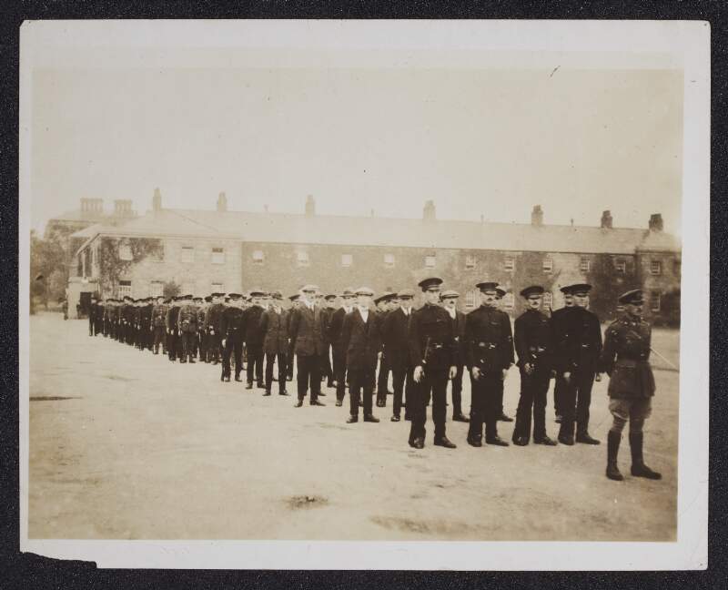 [General John Maxwell [?], with police officers, soliders and civilians, standing in formation within barracks square]