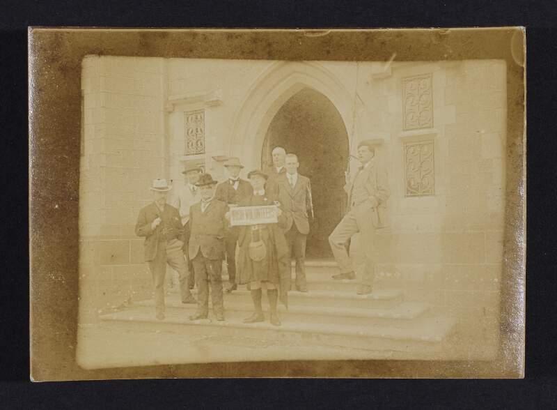 [Men standing outside church entrance one of whom is holding an "Irish Volunteers" sign]
