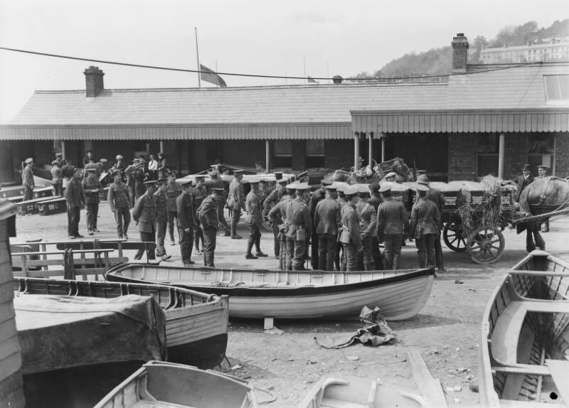 [Lusitania disaster, Cobh, Co. Cork : soldiers gathered around coffins on carts and on the ground, low building in background]