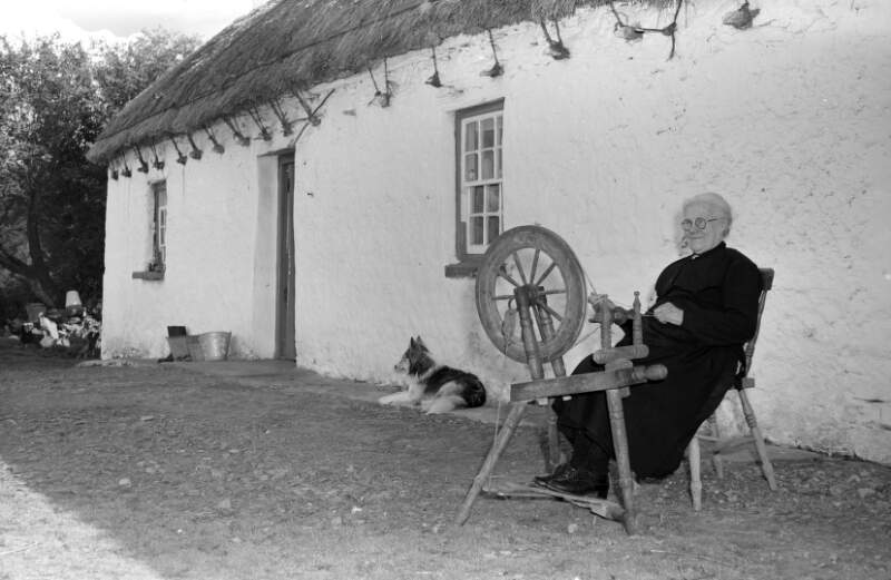 [Elderly woman outside a thatched cottage with a spinning wheel, near Ardara, Co. Donegal]