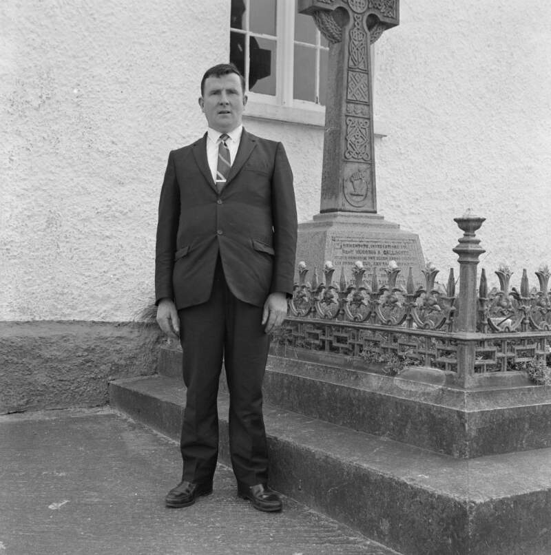 [Man standing beside graveyard during the Easter Parade in Dungloe, Co. Donegal]