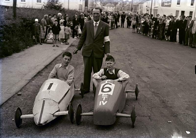 [Man standing behind two boys in go-karts, Co. Donegal]