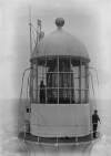 [Lighthouse keeper standing beside the original lantern and optical apparatus of Fastnet Rock, off the coast of Co. Cork]