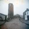 [Commissioners of Irish Lights walking down the main street, with round tower in foreground, Tory Island, off the coast of Co. Donegal]