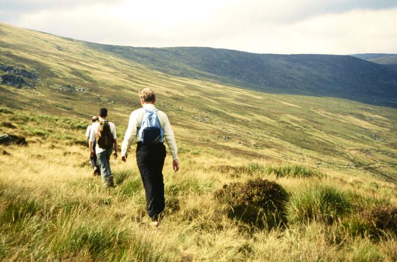 Group walking on grassy foothills. Gay hiking group weekend in Mourne Mountains