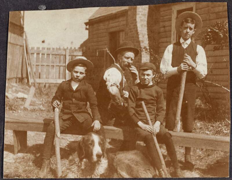 [Photograph of four unidentified men, one older and 3 younger, with a dog]