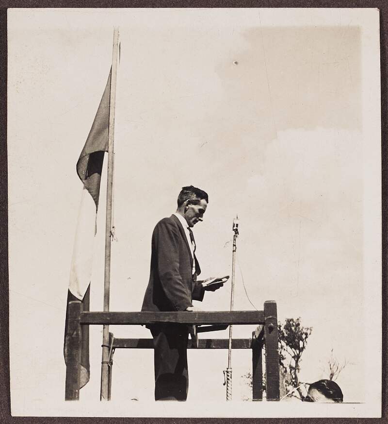 [Man on podium giving a speech, standing beside a tricolour]