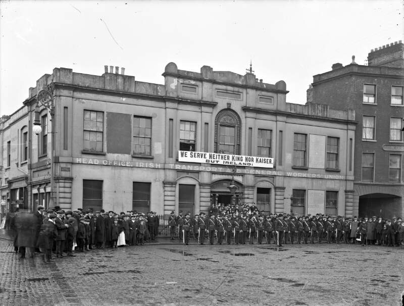[Irish Citizen Army lined up under banner "We Serve Neither King nor Kaiser", outside Liberty Hall, crowd watching the event]