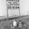[Children seated under traffic sign on shore, ships in background, Pigeon House Road, Ringsend, Dublin]