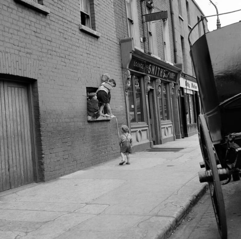 [Children balancing on window ledge near Smith's pub, Bloomsday, Ringsend, Dublin]