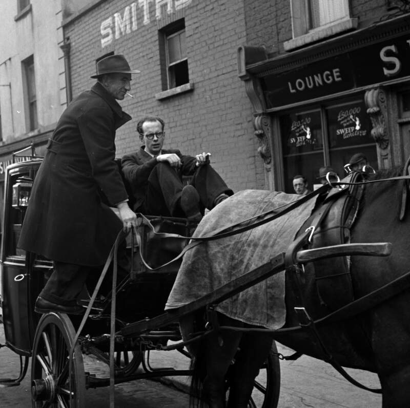 [Anthony Cronin seated on carriage, jarvey dismounting, outside Smith's pub, Bloomsday, Ringsend, Dublin]