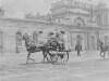 [Horse-drawn jaunting car with passengers, passing Kingsbridge railway station]