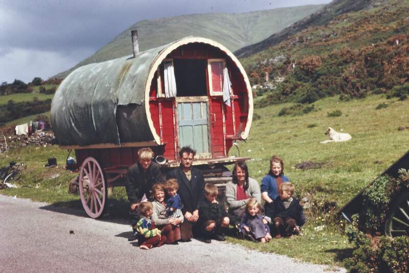 [Irish Traveller family seated outside their caravan]