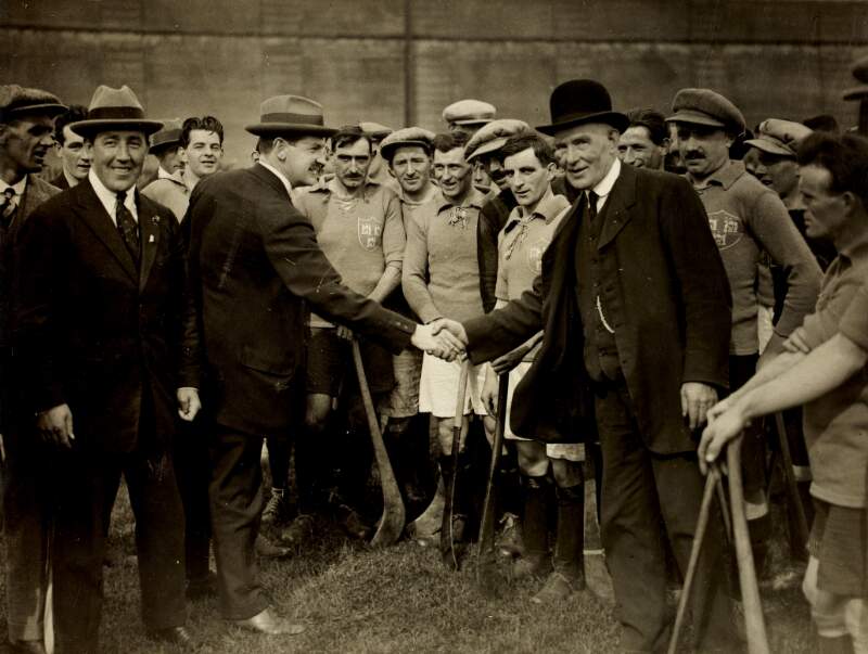 [Michael Collins shaking hands with Alderman James Nowlan (former GAA. President), surrounded by members of the Dublin hurling team at the Leinster Hurling Final in Croke Park]