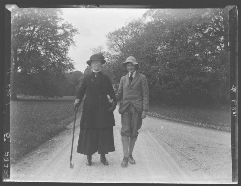 [A.C.C and George. Elderly woman (Augusta Crofton Dillon) and young man walking on gravel drive, he wears floppy hat, she leans on walking stick.]