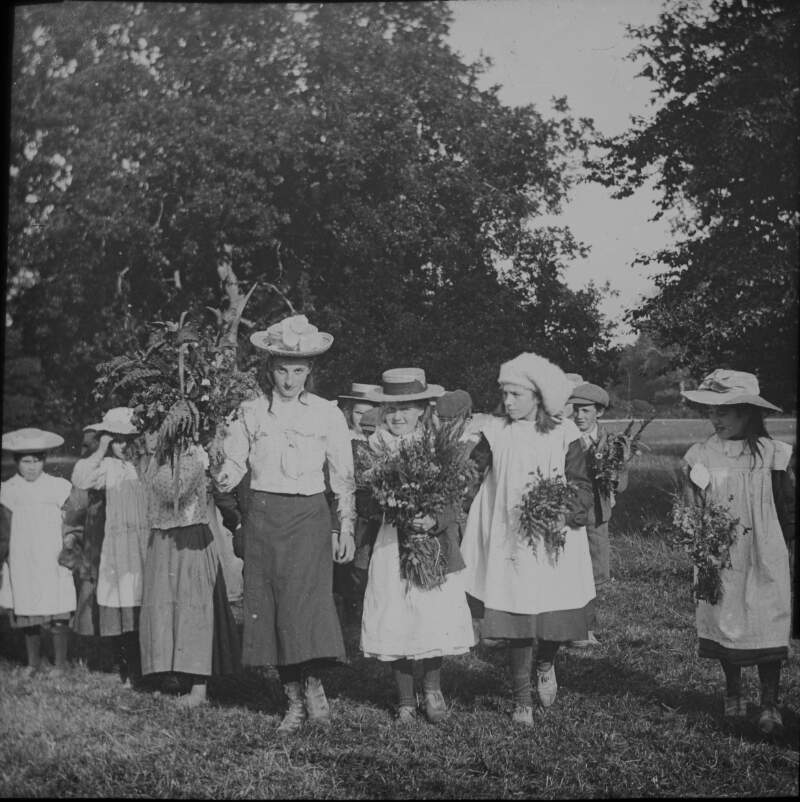 [School treat, Fanny Mason, 1904. Group of school girls dressed in pinafores holding floral bouquets older girl holds larger bouquet, perhaps winner of competition.]