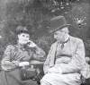 [Luke Gerald Dillon and his wife Augusta Dillon seated outdoors, she is holding a camera.]