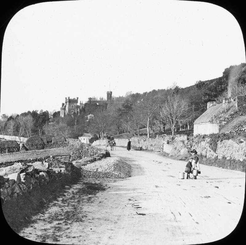 Two girls carry milk pails on the road near Greeba Castle, Isle of Man.