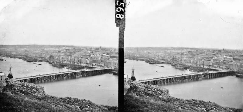 Long shot, high angle, wooden bridge in foreground, quay (many sailing ships) in background, river flowing right to left, Waterford City, Co. Waterford