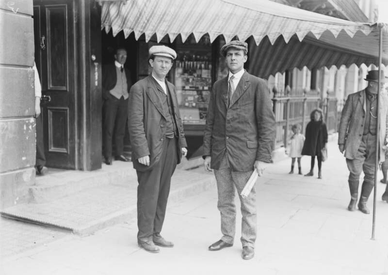 [Survivors of the Lusitania disaster, Cobh, Co. Cork : two men standing in street, under shop awning]