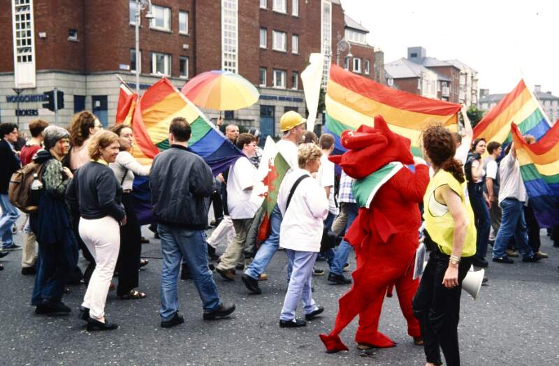 Marchers with rainbow flags and person in red dragon costume. Dublin Lesbian and Gay Pride March