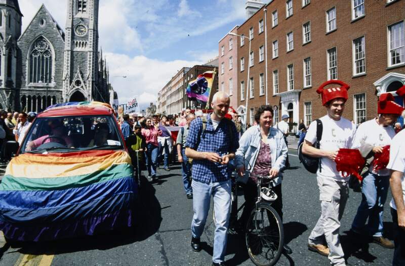 Car draped in rainbow flag among gathering marchers. Dublin Lesbian and Gay Pride March