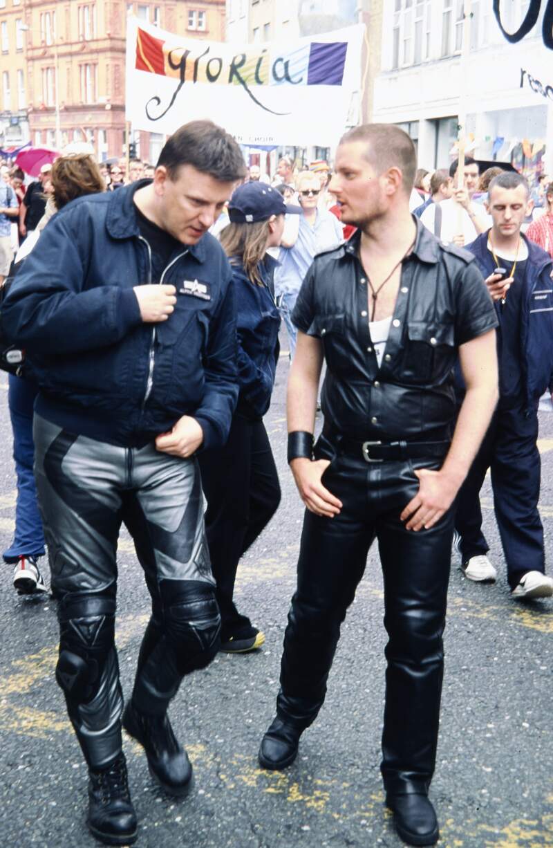 Close up of two men in leather with Gloria banner behind Dublin Lesbian and Gay Pride March